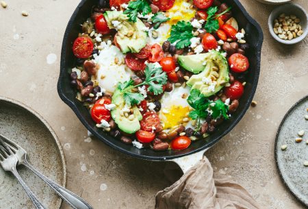 View Mixed bean shakshuka Cast iron skillet sitting on bench top with fresh cooked mixed bean shakshuka, garnished with fresh coriander