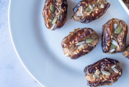 View Nut butter stuffed dates with mixed seeds Plate spread with eight dates, stuffed full with nut butter and mixed seeds