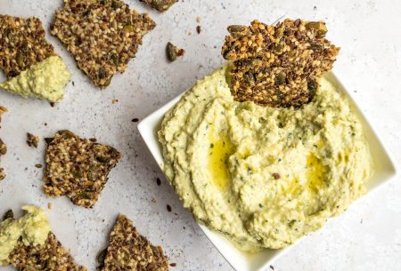 View Creamy artichoke dip One small bowl of creamy artichoke dip, shown on bench top with broken seedy crackers for dipping