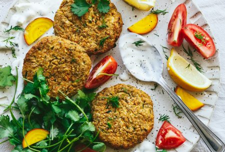 View Courgette & chickpea fritters with probiotic tzatziki One plate with three cooked courgette and chickpea fritters, served with probiotic tzatziki, fresh greens and tomato