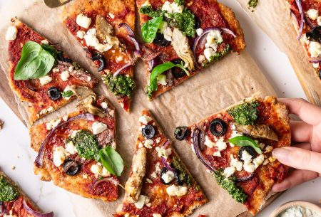 View Fibre-filled wholewheat & bean flatbread pizza A photo of flatbread pizzas on a wooden board. One slice is being grabbed.