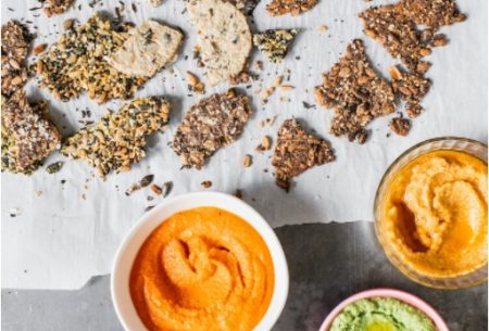 View Harissa red pepper dip Two small pots of harissa red pepper dip, shown on bench top surrounded by mixed broken seed crackers