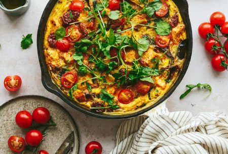View Mediterranean tofu frittata Cast iron skillet with cooked Mediterranean frittata and sundried tomatoes, shown with fresh cherry tomatoes on bench top