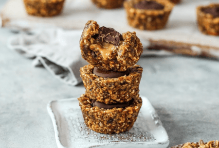 View Dark chocolate & peanut butter granola cups Three dark chocolate and peanut butter granola cups stacked on a small plate, with seven more scattered on bench top in background