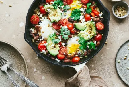 View Mixed bean shakshuka Cast iron skillet sitting on bench top with fresh cooked mixed bean shakshuka, garnished with fresh coriander