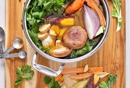 View Busting the bone broth myth A wooden board with a pot of vegetables and broth and herbs inside