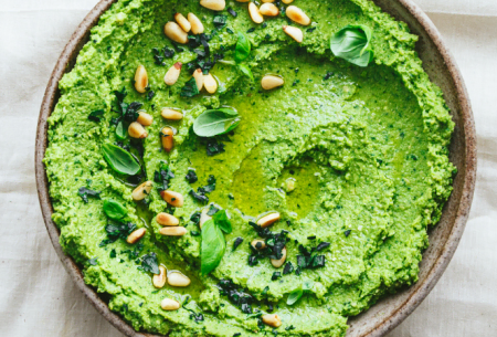 View Leafy green pesto hummus Bowl of bright green leafy pesto hummus, sprinkled with pine nuts and fresh basil leaves