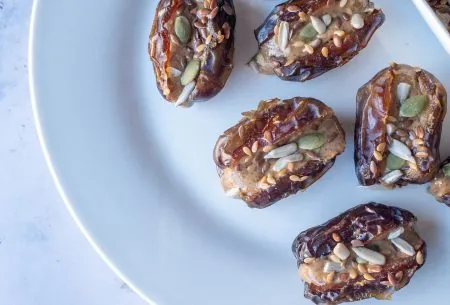 View Nut butter stuffed dates with mixed seeds Plate spread with eight dates, stuffed full with nut butter and mixed seeds