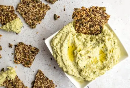 View Creamy artichoke dip One small bowl of creamy artichoke dip, shown on bench top with broken seedy crackers for dipping