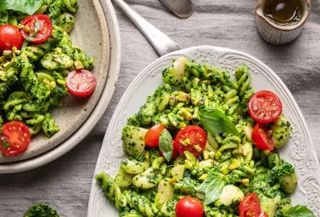 View Cavolo nero and pistachio pesto pasta with butter beans A photo of pesto pasta on two plates laid on a table