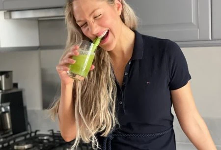 View Celery juice: myths vs reality Dr Megan Rossi standing in a kitchen holding a celery juice up to her mouth and laughing