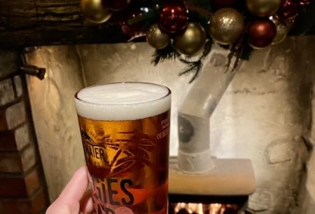 View Alcohol & the gut One hand holding up a glass full with beer, festive fireplace and decorations shown in background