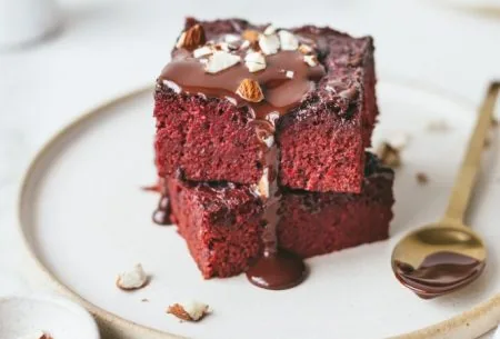 View Prebiotic beet velvet brownies Two prebiotic beet velvet brownies stacked on a plate with melted chocolate and crushed almonds