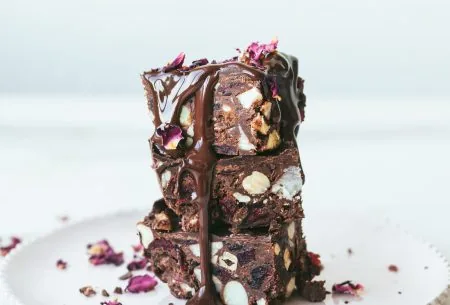 View Fruit & nut love bites Three fruit and nut chocolate bites stacked on a white plate, drizzled with chocolate and garnished with small rose petals
