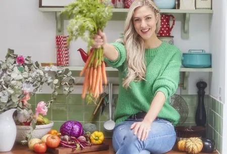 View World Food Day! Megan Rossi sat on kitchen surface holding a bunch of carrots