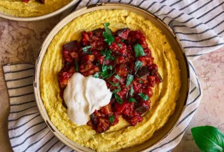 View Sweetcorn polenta with aubergine ragu Bowl of sweetcorn polenta topped with aubergine ragu, chopped basil and a dollop of yogurt