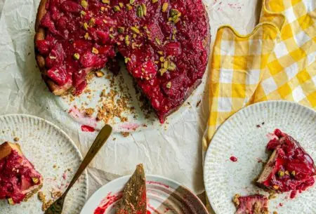 View Pistachio and strawberry baked cheesecake Photo of strawberry and pistachio cheesecake and two plates with slices of cheesecake that are half eaten