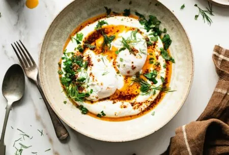 View Prebiotic Turkish eggs A bowl of prebiotic Turkish eggs topped with sprigs of dill and mint and a drizzle of chilli oil.