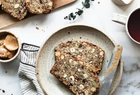 View Nordic style super seedy & nutty loaf with figs Two pieces of Nordic style super seedy and nutty loaf with figs, with knife and nut butter spread