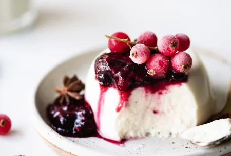 View Live panna cotta with mulled berry compote One serve of live panna cotta with mulled berry compote on top and frozen berries, served on a small ceramic plate
