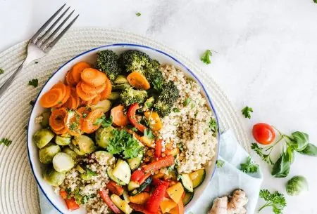 View Why veg & grains are essential for your gut microbes A colourful bowl of food including quinoa, roasted mixed peppers, courgette, carrot, brussell sprouts and broccoli on a place mat with a napkin and piece of ginger