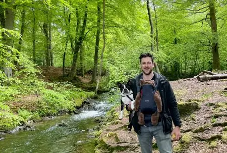View Paternal programming: how it works Man with baby strapped to chest, standing outdoors in a green forest by a small river