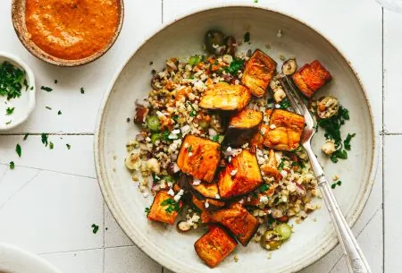 View Roast aubergine with grains & red pepper sauce Roast aubergine with mixed grains and red pepper sauce, on a white place with a pot of extra sauce