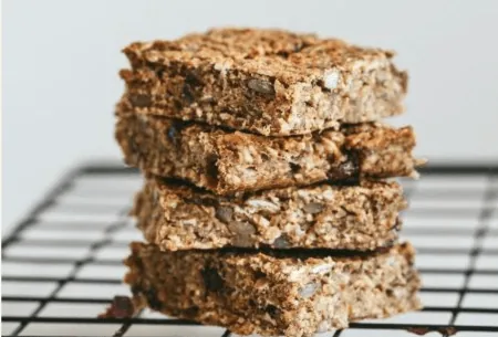 View Nutty banana fibre-filled flapjacks Four nutty banana fibre-filled flapjacks stacked on a wire cooling rack