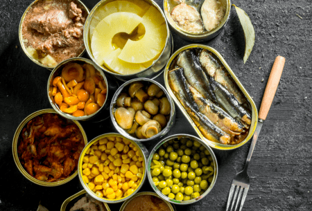 View Is canned food OK to eat? Bench top with large variety of canned foods on display, all with tops off to show food inside