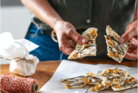 View Prebiotic chocolate bark One large piece of prebiotic chocolate bark being broken in half, topped with mango, pistachios and dark chocolate