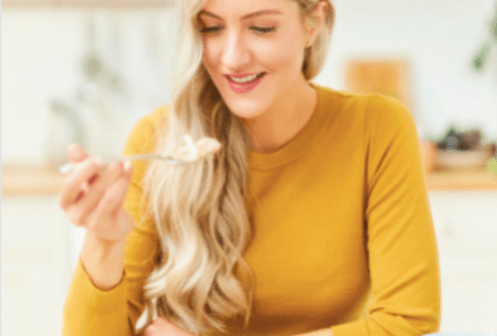 View Science-backed benefits of porridge Dr Megan Rossi wearing a yellow shirt, sitting in front of a bowl of porridge while lifting a spoon to her mouth