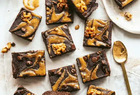 View Fudgy black bean & walnut brownies 12 fudgy black bean and walnut brownies scattered on a bench top, drizzled with walnut butter