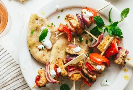 View Spiced tofu skewers with mint yoghurt Two spiced tofu skewers with mint yoghurt, shown on white plate with torn flatbread