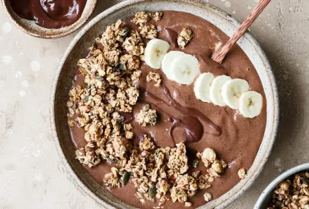View Chocolate & banana smoothie bowl Chocolate and banana smoothie bowl topped with extra granola and banana, and a small pot of extra chocolate